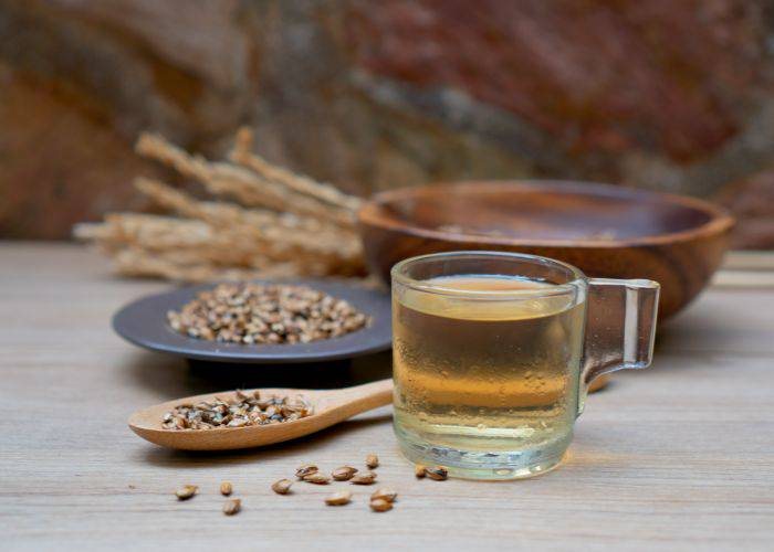 A glass mug of barley tea with barley kernels in the background.